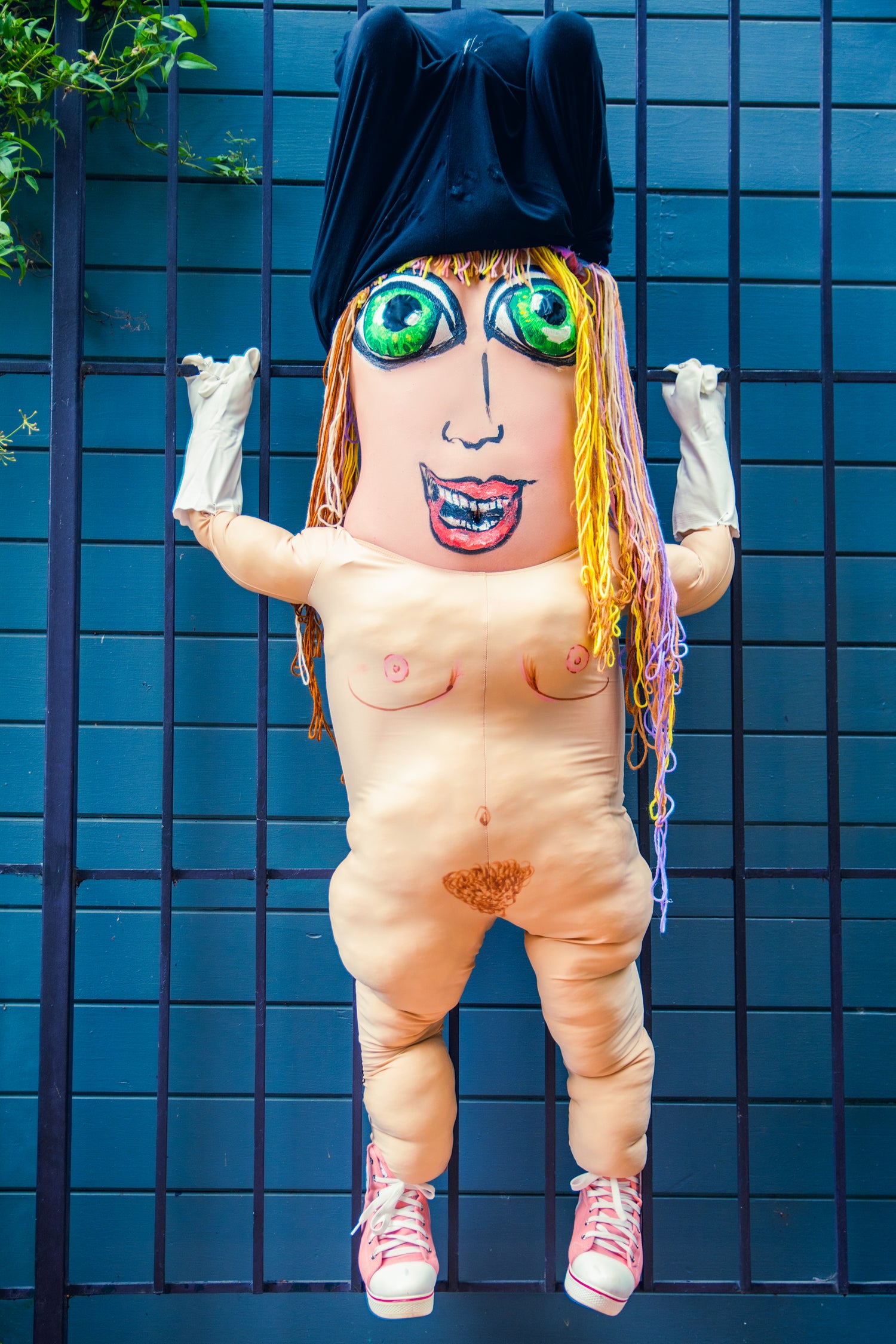 A person with their breasts painted like eyes appears with their arms over their head, covered with a black piece of material. A bodysuit that places arms on the persons hips helps to create an illusion of a comical creature that we recognize but not.